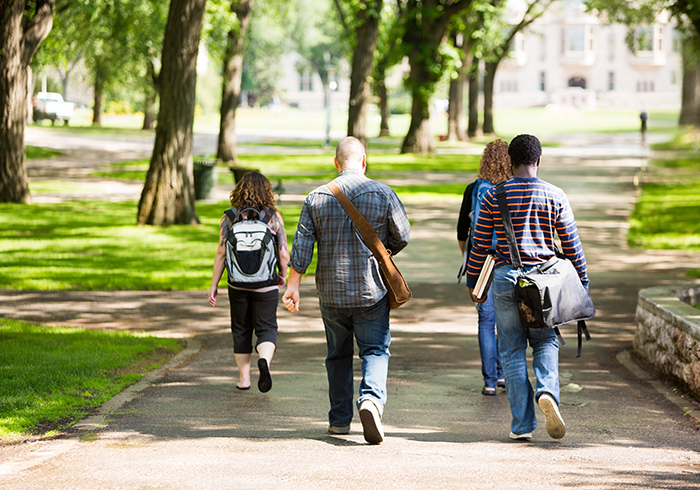 Students walking away down a college campus path through a greenspace