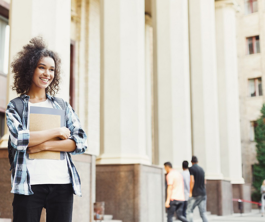 Person standign outside a university with books in their arms